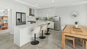 Eine moderne Küche mit einer zentralen Kochinsel, weißen Schränken, Edelstahlgeräten und einem Essbereich mit Holztisch und Stühlen.