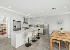Eine moderne Küche mit einer zentralen Kochinsel, weißen Schränken, Edelstahlgeräten und einem Essbereich mit Holztisch und Stühlen.
