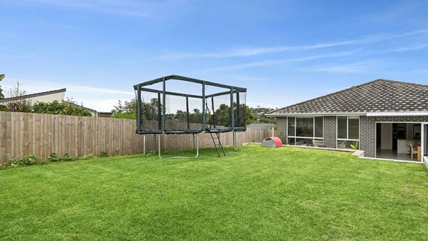 Ein Garten mit Trampolin, Holzzaun und einem Haus mit Ziegeldach.
