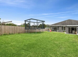 A backyard with a trampoline, a wooden fence, and a house with a tiled roof. - Manly 3km I Modern 5BR Retreat | Pool | Sleeps 13 (Allambie Heights)