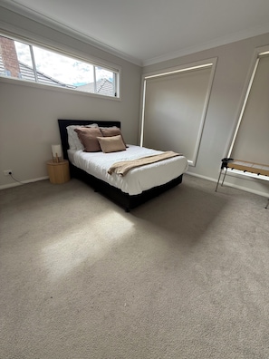 Un dormitorio con cama, ventana, radiador y estante fijado a la pared.