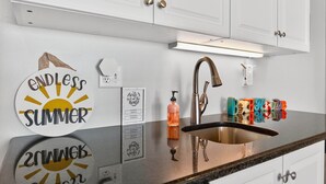 Een keuken met witte kastjes, een roestvrijstalen spoelbak en decoratieve muurstickers.
