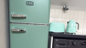 Une cuisine de taille réduite avec un réfrigérateur de couleur turquoise, un lave-linge noir et un pare-feu en carreaux.