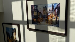 Deux tableaux encadrés représentant une scène de rue avec des bâtiments et une tour, accrochés à un mur.