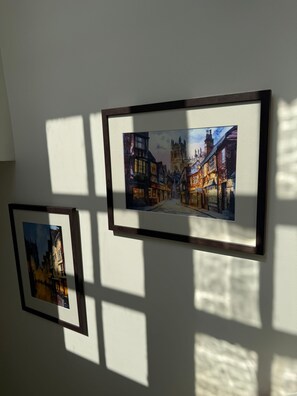Zwei gerahmte Gemälde zeigen eine Straßenszene mit Gebäuden und einem Turm, die an einer Wand angebracht sind.