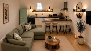 Une cuisine moderne avec un réfrigérateur vert, un coin repas doté d’un tabouret de bar et un salon avec un canapé d’angle.