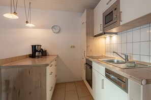 A modern kitchen with wooden cabinets, a stainless steel sink, and a microwave. - Gemutlicher Doppelbungalow mit Garten und Terrasse im Ferienpark Mirow (Mirow)