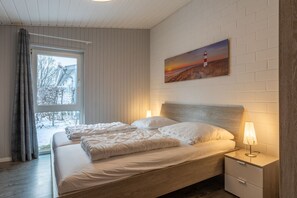 A bedroom with a bed, a nightstand, a painting, and a window with curtains. - Gemutlicher Doppelbungalow mit Garten und Terrasse im Ferienpark Mirow (Mirow)