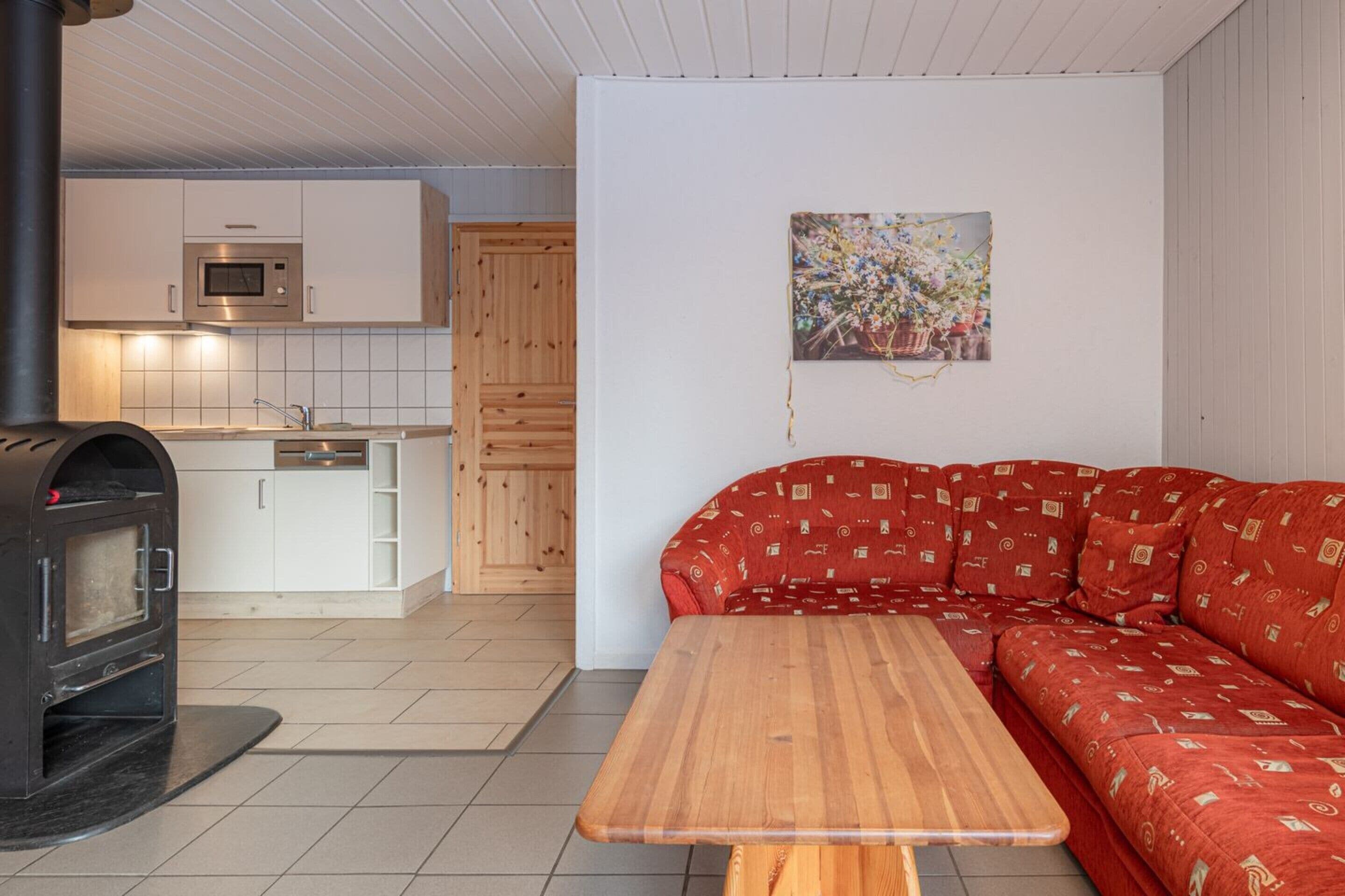 Eine moderne Küche mit weißen Schränken, einer Mikrowelle und einem eingebauten Backofen. Im Wohnbereich befindet sich eine Holzbank und ein rot gemustertes Sofa.