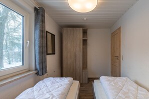 A narrow room with two beds, a wardrobe, and a window with a curtain. - Gemutlicher Doppelbungalow mit Garten und Terrasse im Ferienpark Mirow (Mirow)