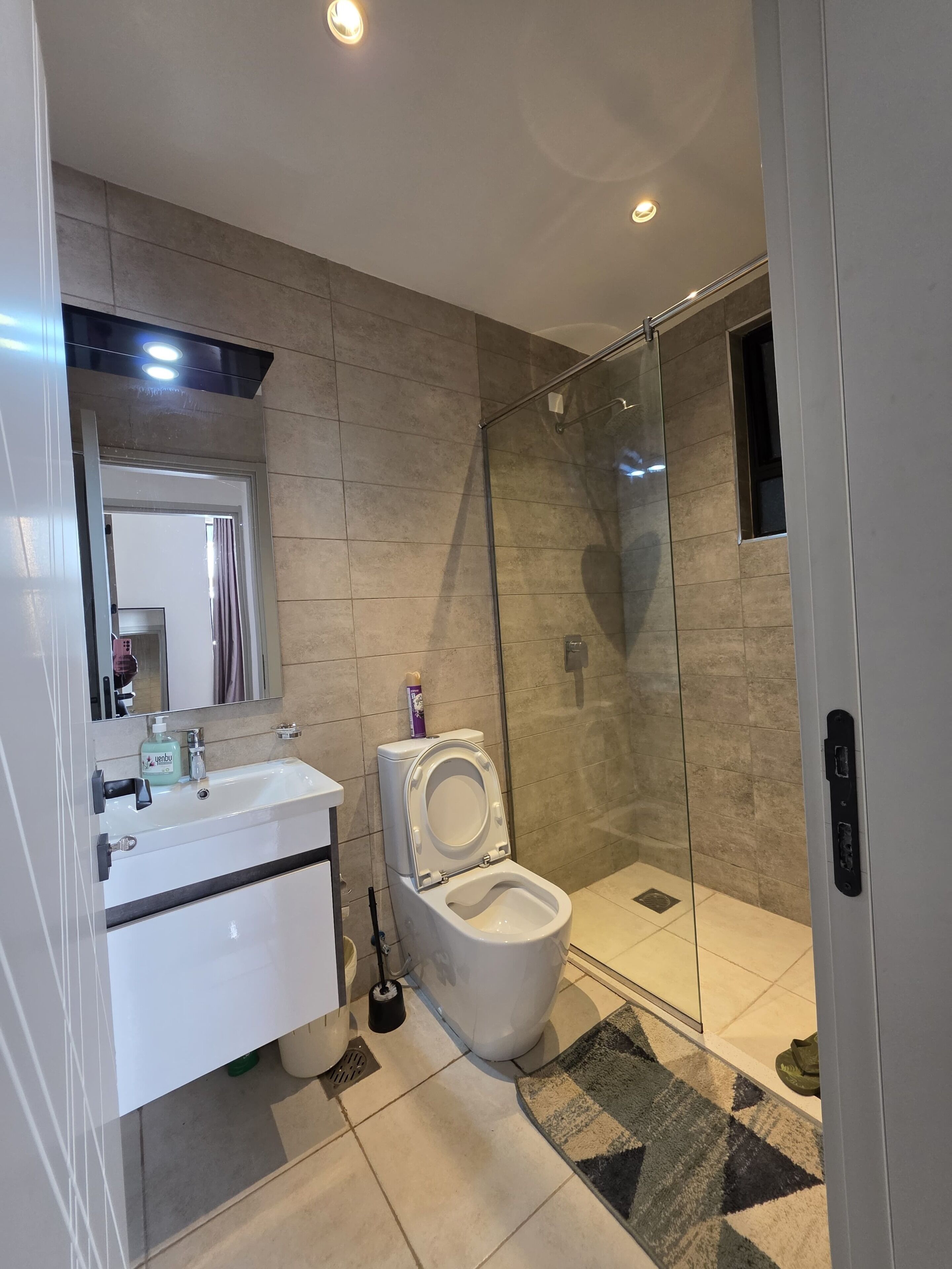 Ein modernes Badezimmer mit Duschkabine aus Glas, Waschbecken mit Spiegel und Toilette.