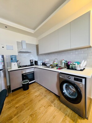 A compact kitchen with a washing machine, a sink, and a stove. -  3-bedroom apartment in lovely Nairobi with sauna & SPA (Nairobi)