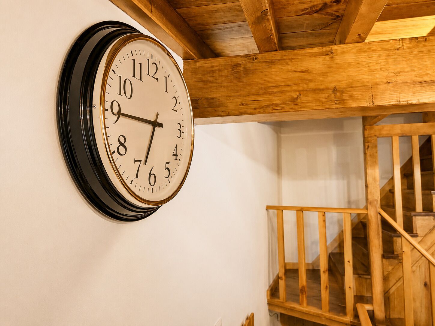 Un reloj de pared con esfera blanca y números negros, situado sobre una escalera de madera.