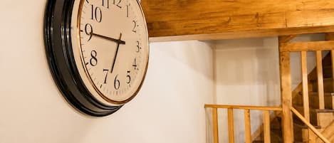Un reloj de pared con esfera blanca y números negros, situado sobre una escalera de madera.