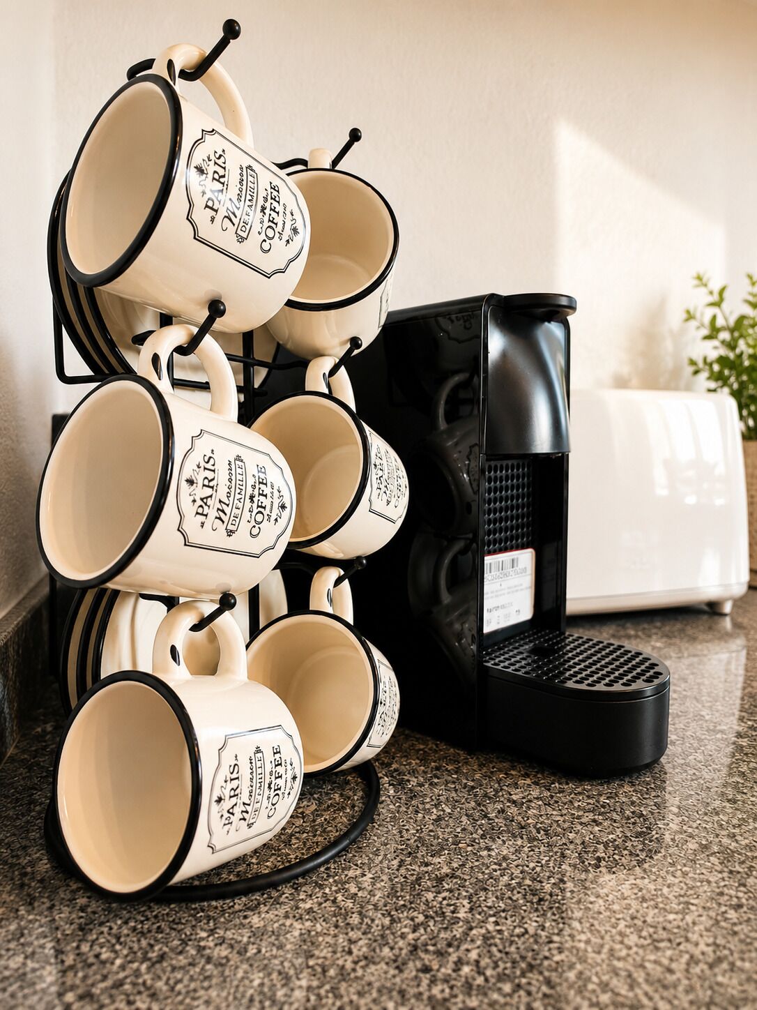 Una pila de tazas de café con la palabra 'Paris' y 'Coffee', una cafetera negra y un electrodoméstico blanco sobre una encimera de cocina.