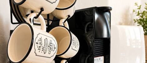 Una pila de tazas de café con la palabra 'Paris' y 'Coffee', una cafetera negra y un electrodoméstico blanco sobre una encimera de cocina.