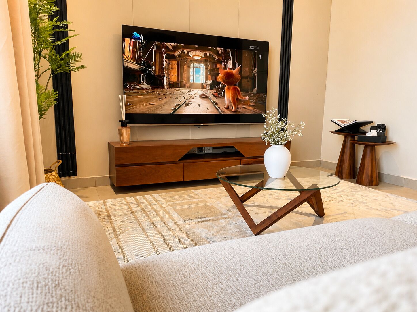 Una sala de estar moderna con un televisor de pantalla plana, una mesa de centro de vidrio, un sofá y un jarrón decorativo.