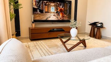 Una sala de estar moderna con un televisor de pantalla plana, una mesa de centro de vidrio, un sofá y un jarrón decorativo.