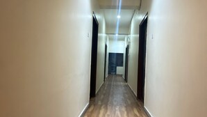 A long, narrow hallway with wooden flooring and white walls, leading to a dark room at the end. - A.V Grand Hotel (Kanpur)