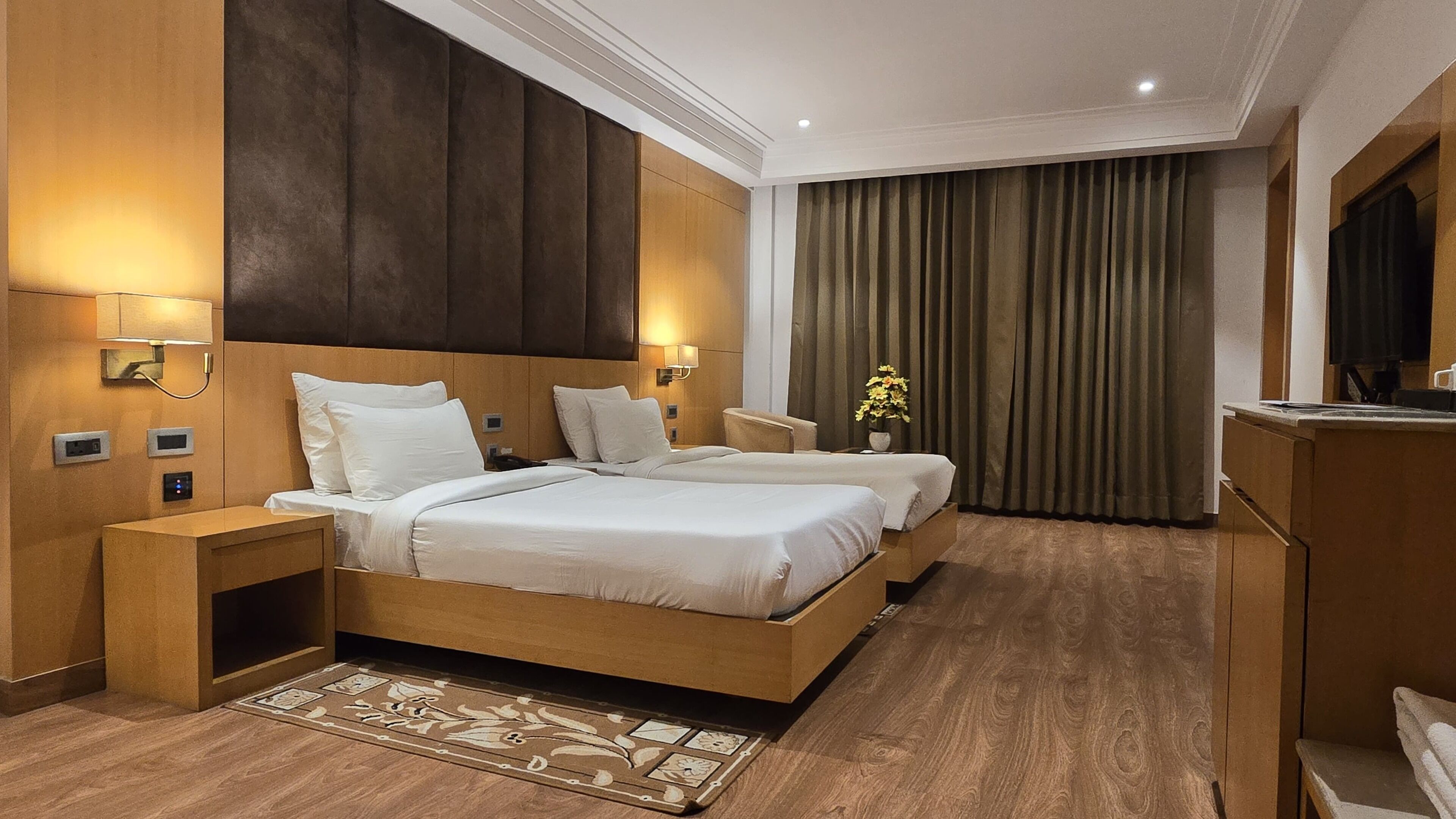 A hotel room with two beds, a desk, a TV, and a bathroom.