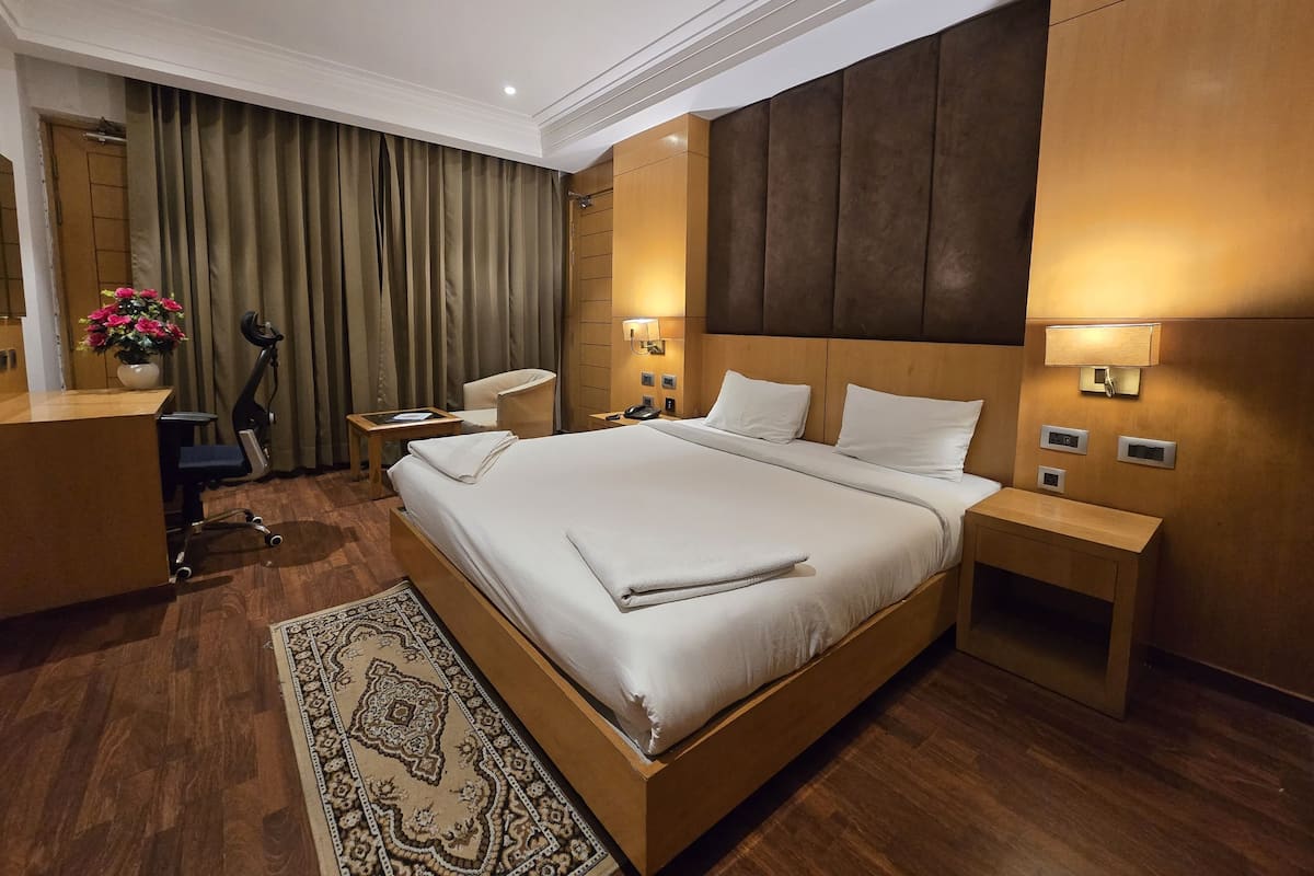 Een hotelkamer met een groot bed, een bureau, een stoel, een bureaulamp, een nachtkastje en een wandlamp.