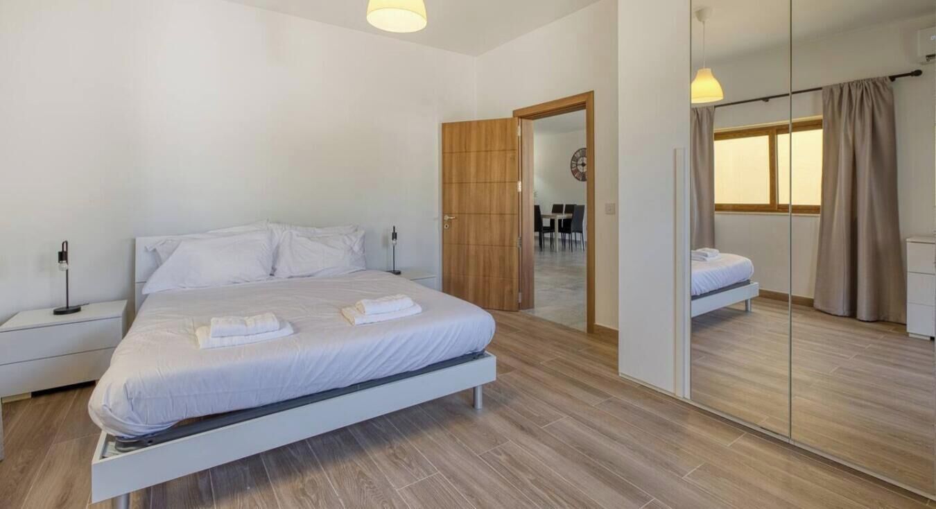 Un dormitorio moderno con una cama grande, mesitas de noche, un espejo y vistas a un comedor.