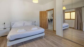 Un dormitorio moderno con una cama grande, mesitas de noche, un espejo y vistas a un comedor.