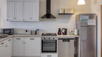 Una cocina moderna con armarios blancos, horno empotrado, lavavajillas, microondas, cocina a gas y refrigerador.