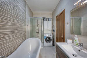 Een moderne badkamer met een vrijstaand bad, een douchecabine, een ingebouwde wasmachine en een grote spiegel boven de wastafel.