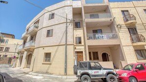 A multi-story building with balconies, a parked off-road vehicle, and a red car. - Fully equipped 3BR Mosta home, Rotunda View w/WIFI (Mosta)