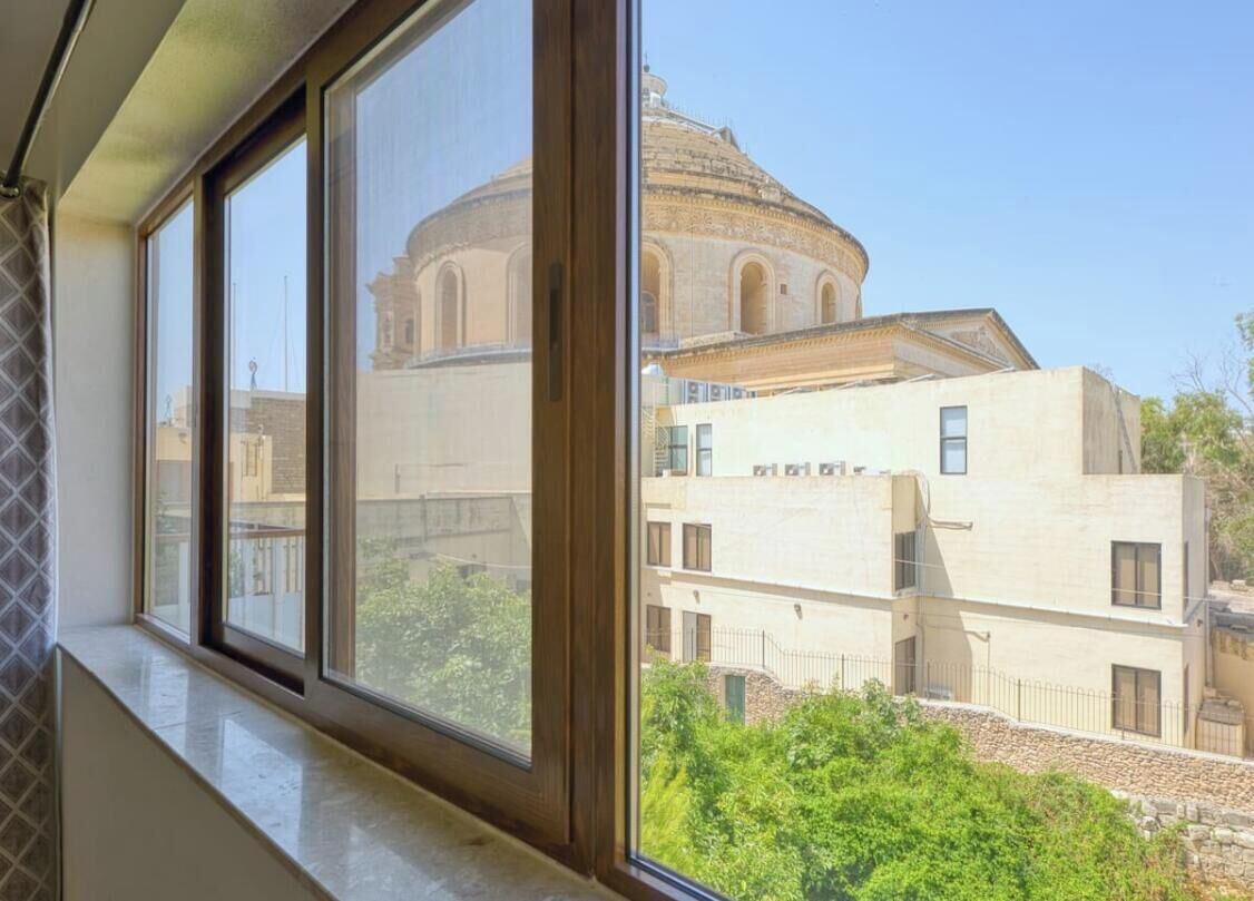 Vista dalla finestra su un edificio con una cupola e una struttura moderna in primo piano.