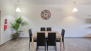 A conference room with a wooden table, black chairs, a wall-mounted clock, pendant lights, and a potted plant. - Fully equipped 3BR Mosta home, Rotunda View w/WIFI (Mosta)