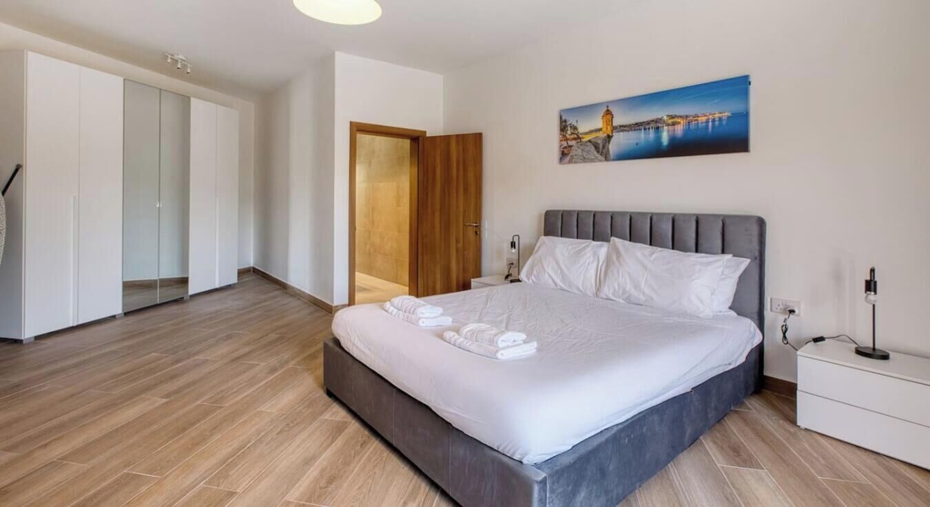 A bedroom with a bed, a nightstand, a wall-mounted picture, and a wardrobe.