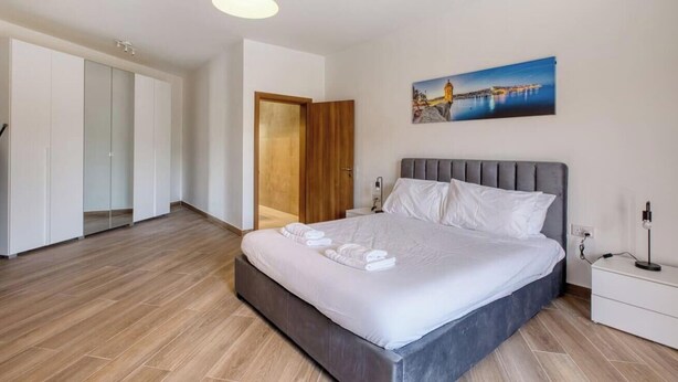 A bedroom with a bed, a nightstand, a wall-mounted picture, and a wardrobe. - Fully equipped 3BR Mosta home, Rotunda View w/WIFI (Mosta)
