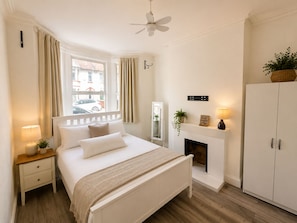 A bedroom with a bed, bedside table, lamp, curtains, a fireplace, and a wardrobe. - Generous 4BDR Modern Family Home in Ilford Lane (Greater London)
