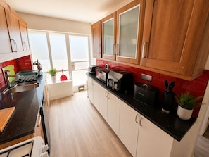A modern kitchen with wooden cabinets, a black countertop, and a red backsplash. - Generous 4BDR Modern Family Home in Ilford Lane (Greater London)