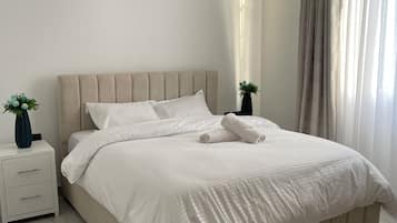 A neatly made bed with white linens, a bedside table with a vase, and a wall-mounted light fixture.