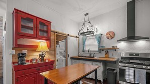 Et køkken med et træbord, røde skabe, en komfur og en hængende lampe.