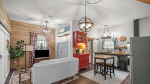 Un espace de vie compact comprenant un canapé, un téléviseur, des murs en bois, un coin cuisine et une table à manger.