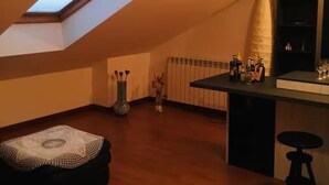 Um quarto com teto inclinado, claraboia, pequeno bar, um banquinho redondo e um vaso decorativo.