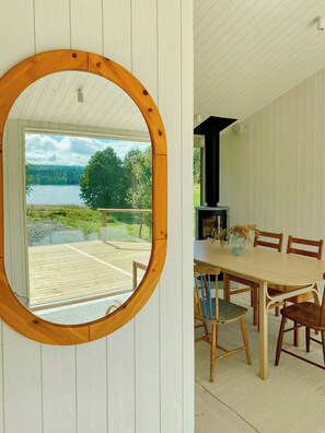 Un espejo de madera, una mesa de comedor con sillas y vistas a un lago y un bosque a través de un ventanal grande.