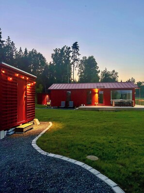 Un edificio rojo con techo de metal, una zona de estar al aire libre cubierta y un césped bien cuidado.