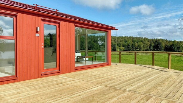 Ein rotes Holzgebäude mit großen Glasfenstern und einer Terrasse.