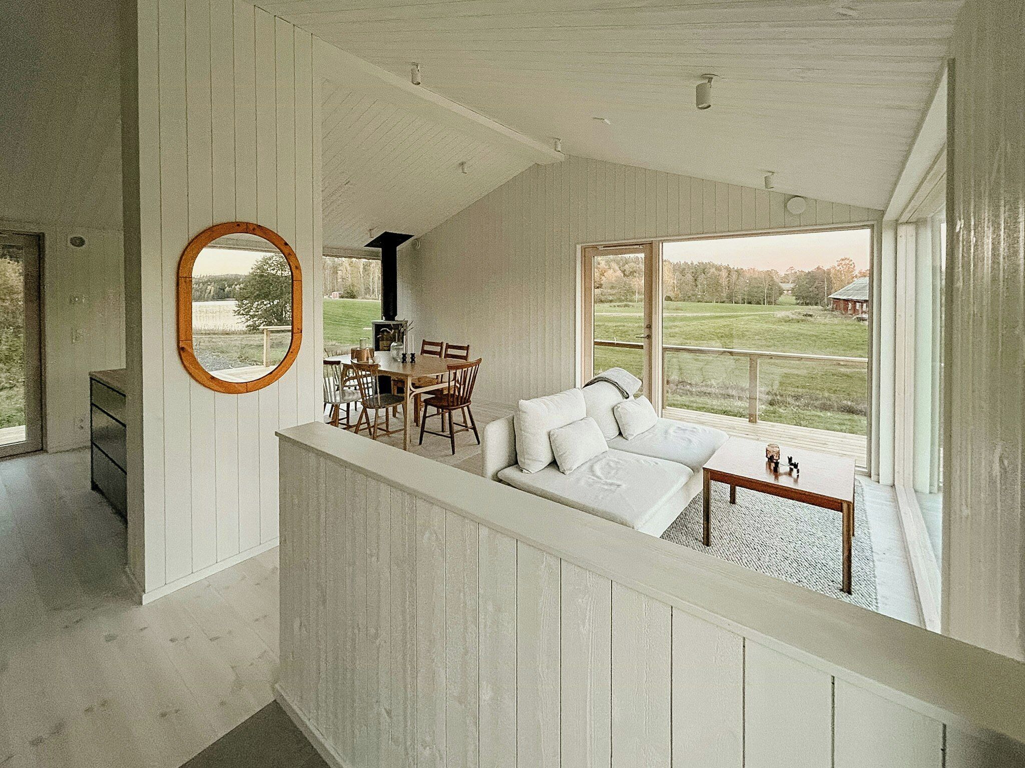 A spacious room with a dining area, a white sofa, and large windows offering a view of the outdoors.