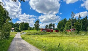 A rural landscape with a gravel path leading to a red building surrounded by greenery and trees. - Bright summer house by Klocksjön in Ramkvilla (Ramkvilla)