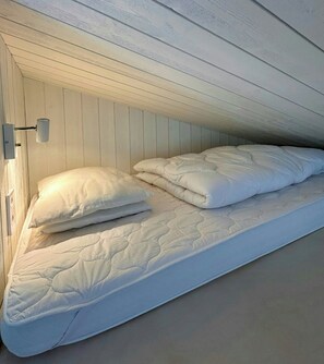 Uma cama de solteiro com colchão e almofadas em quarto com painéis de madeira nas paredes.