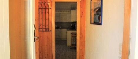 Un couloir étroit avec une porte en bois donnant sur un espace cuisine.