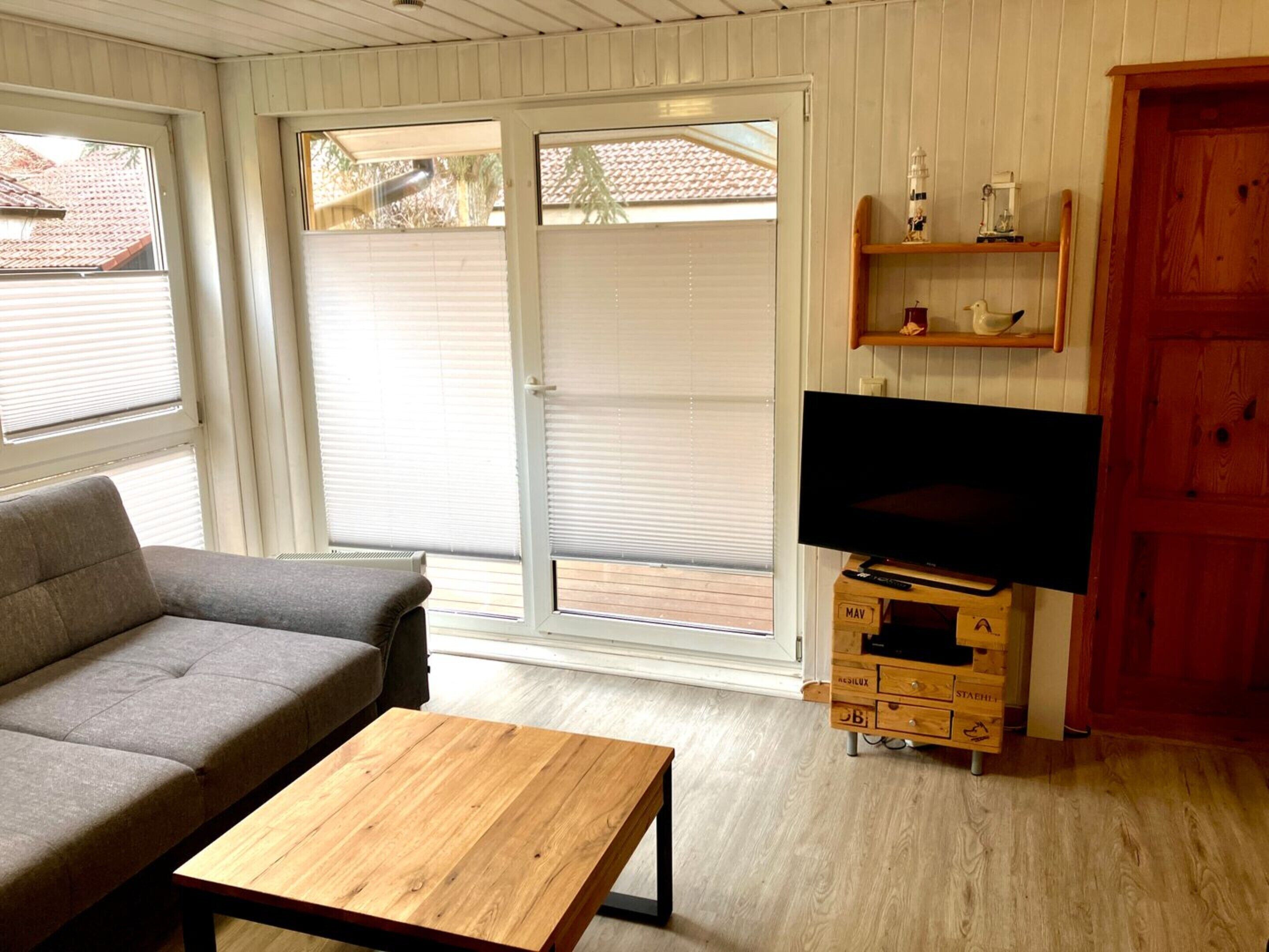 A living room with a sofa, a coffee table, a television on a wooden stand, and a sliding glass door leading to an outdoor area.