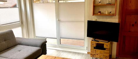 A living room with a sofa, a coffee table, a television on a wooden stand, and a sliding glass door leading to an outdoor area.