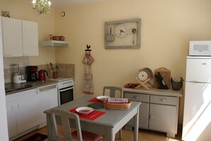 A compact kitchen with white cabinets, a dining table with chairs, a microwave, and a refrigerator. - Gîte le lit de la loire (Varennes-sur-Loire)